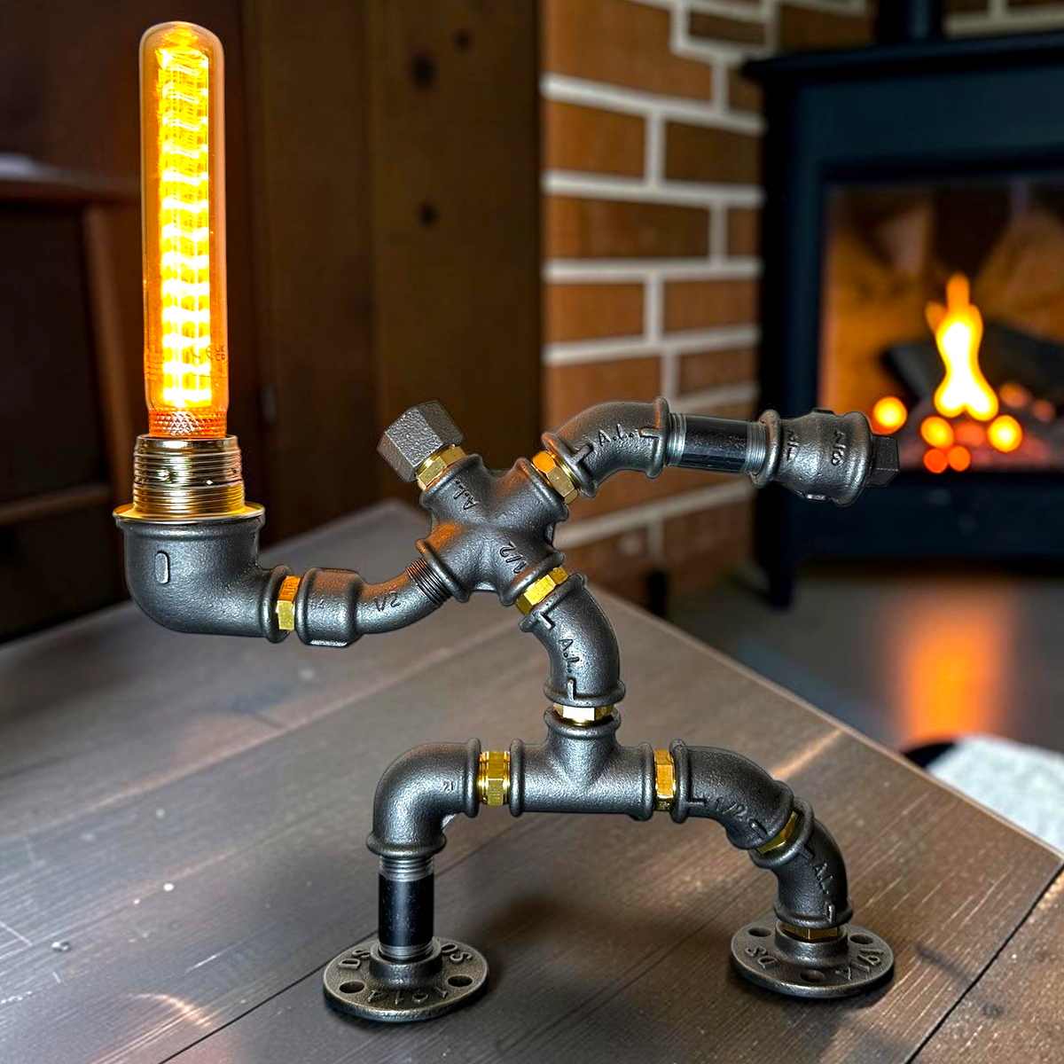 KerleKiste Hampelmann Tischlampe aus schwarzem Industrierohr mit Edison-Glühbirne vor einem Kamin